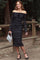 woman wearing a black off-the-shoulder lace midi dress with long sleeves and a fitted silhouette, standing outdoors