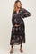 woman wearing a flowy dark floral maternity dress with long sleeves and tiered design, holding her baby bump