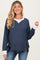 woman wearing a navy blue waffle knit maternity top with light gray trim and side slits, smiling at the camera