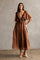 woman wearing a brown tiered maxi dress with ruffled sleeves and a tie waist, standing against a textured wall