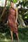 woman wearing a one-shoulder ruched midi dress in brown and pink tones with floral detailing, standing in a garden setting