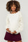 woman wearing a cream maternity sweater with decorative sleeves and holding her baby bump
