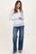 woman wearing a light blue maternity long sleeve top with scalloped details and blue wide-leg jeans, holding a white handbag