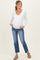 woman wearing a white long sleeve maternity top and blue jeans, showing her baby bump