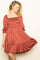 woman wearing a rust-colored smocked sundress with puff sleeves and a tiered skirt