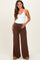 woman wearing a white maternity bodysuit and brown wide-leg maternity pants, showing her baby bump