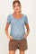 woman wearing a light blue short sleeve maternity top with floral print and a visible baby bump, paired with brown shorts