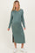 woman wearing a green long sleeve maternity dress with a side slit and pocket, showcasing her baby bump