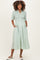 woman wearing a light green maternity dress with a button front and pockets, styled with short sleeves and a smocked bodice