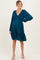 woman wearing a teal maternity dress with a deep v-neck, long sleeves, and a ruffled hem, showing her baby bump