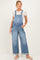 woman wearing a light blue maternity denim overalls with a white t-shirt underneath and standing casually