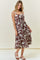 woman wearing a brown and cream floral print midi dress with straps and a flared skirt, standing with one hand on her hip
