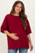 woman wearing a burgundy oversized maternity top and holding her baby bump