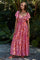 woman wearing a pink floral maxi dress with short ruffled sleeves standing outdoors among greenery