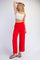 woman wearing a white cropped tank top and red wide-leg pants, standing with one hand on her hip