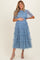 woman wearing a light blue maternity dress with tiered tulle layers and short sleeves, holding her baby bump