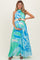 woman wearing a blue and green floral maternity maxi dress, holding her baby bump and styled with a belted waist