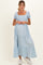 woman wearing a light blue maternity dress with puff sleeves and a tiered skirt, holding her baby bump