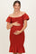 woman wearing a rust off-shoulder maternity dress with puff sleeves and a ruffled hem, cradling her baby bump