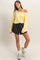 woman wearing a yellow off-shoulder long sleeve top and black drawstring shorts, styled with white socks and sneakers