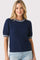 woman wearing a navy short sleeve sweater with a textured knit and striped neckline, paired with distressed denim shorts
