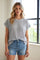 woman wearing a light gray short sleeve top with textured stripes and denim shorts