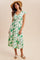 woman wearing a white floral midi dress with green accents and cap sleeves, paired with a straw hat and espadrilles