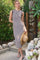 woman wearing a striped sleeveless midi dress with a button detail, holding a straw hat in a garden setting