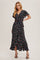 woman wearing a black floral wrap dress with ruffled sleeves and a high low hemline, standing confidently