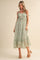 woman wearing a green floral maxi dress with ruffled details and tie straps, standing on a neutral background