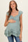 woman wearing a sage green maternity top with ruffles and short sleeves, holding her baby bump