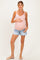 woman wearing a light pink maternity tank top and denim shorts, holding her baby bump