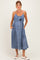 woman wearing a light blue denim maternity dress with a tie waist and pockets, showcasing her baby bump