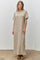 woman wearing a beige striped maxi dress with scalloped edges and side slits, standing on a concrete floor