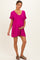 woman wearing a bright pink maternity dress with a v-neck and short sleeves, gently holding her baby bump