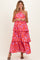 woman wearing a strapless red floral maxi maternity dress with layered tiers and smiling at the camera