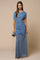 woman wearing a blue ruched evening gown with a sheer overlay and cap sleeves, holding a clutch handbag