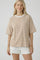 woman wearing a beige and white striped oversized t-shirt with short sleeves and standing with a slight smile