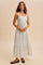 woman wearing a white maxi dress with black polka dots and a tiered hem, standing on a neutral background