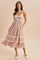 woman wearing a pink floral maxi dress with lace trim and pockets, standing against a neutral background