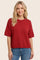 woman wearing a red short sleeve knit sweater with a relaxed fit and round neckline, styled with blue jeans