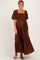 woman wearing a brown smocked maternity maxi dress with puff sleeves and lace detailing, showcasing her baby bump