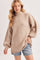 woman wearing a beige oversized knit sweater with a high neck and balloon sleeves, paired with denim shorts