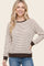 woman wearing a striped cream and brown long sleeve sweater with a relaxed fit and ribbed cuffs