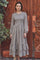 woman wearing a gray long sleeve dress with ruffled hem and smocked bodice in a floral print standing in front of wooden doors