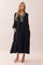 woman wearing a black tiered maxi dress with long sleeves and decorative detailing on the neckline and cuffs