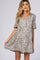 woman wearing a cream and black spotted maternity dress with a v-neck and short sleeves, holding the skirt gently