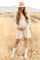 Pregnant woman in a linen dress and wide brim hat standing in a golden field during a maternity photoshoot