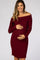 smiling pregnant woman wearing a burgundy off-the-shoulder ribbed maternity dress holding her baby bump