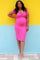 Smiling pregnant woman in a pink maternity dress posing against a yellow and blue wall